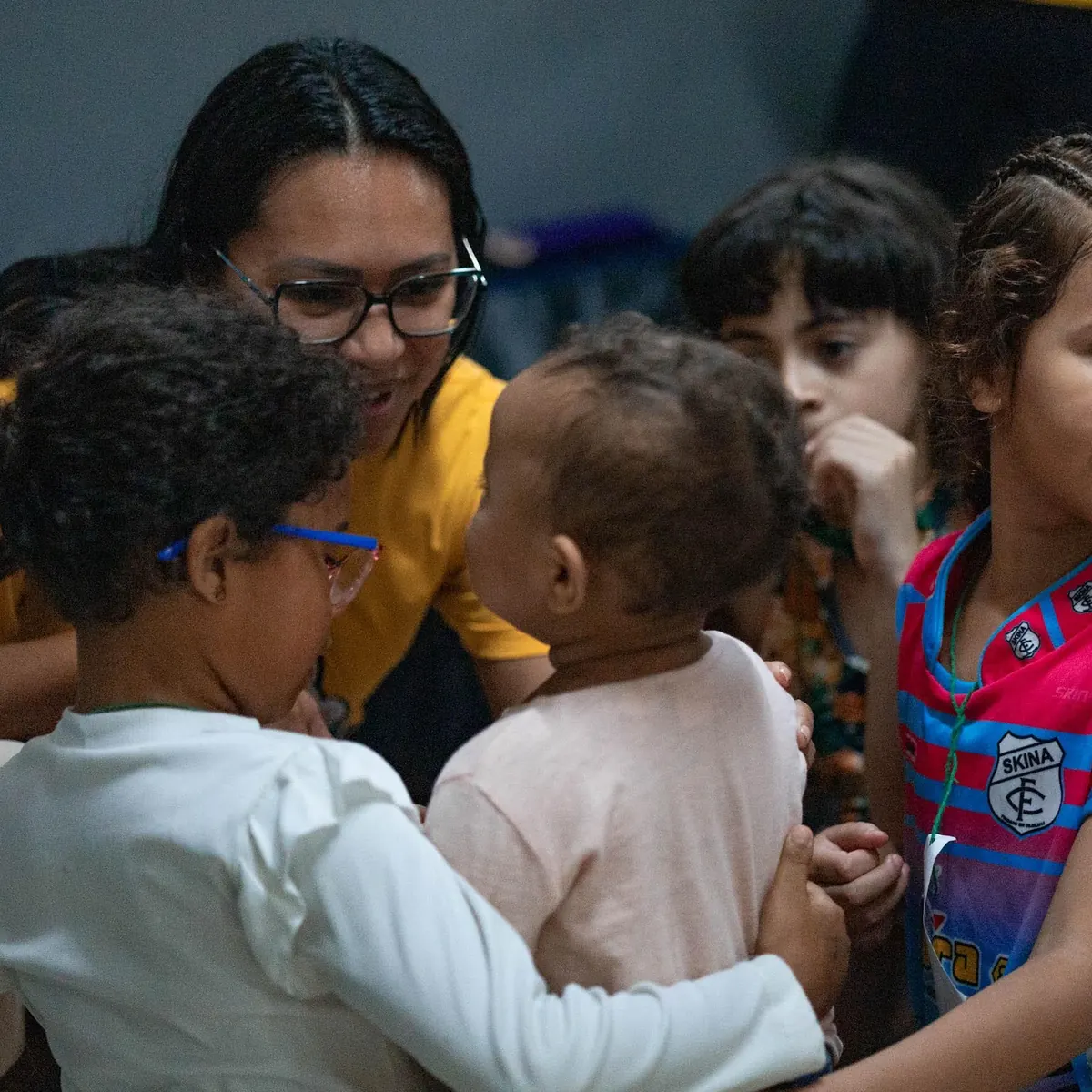 Voluntária abraçando crianças pequenas no AcampaKids