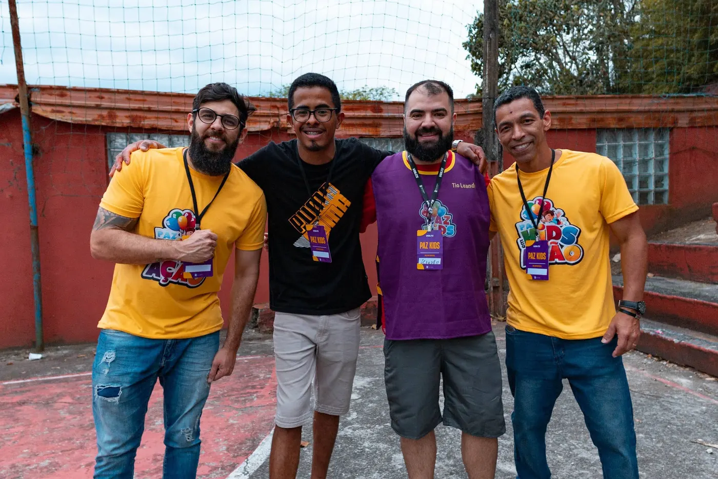 Quatro voluntários do Paz Kids em Ação abraçados na quadra do AcampaKids