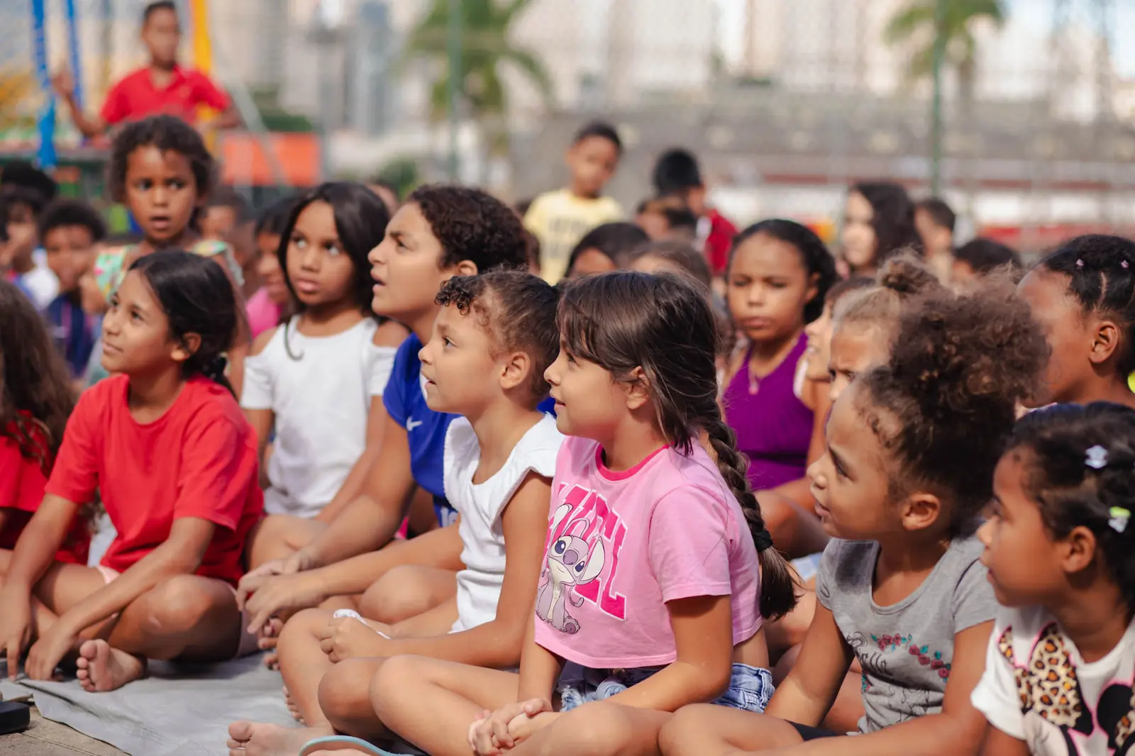 Crianças sentadas no chão prestando atenção numa ação do Paz Kids em Ação
